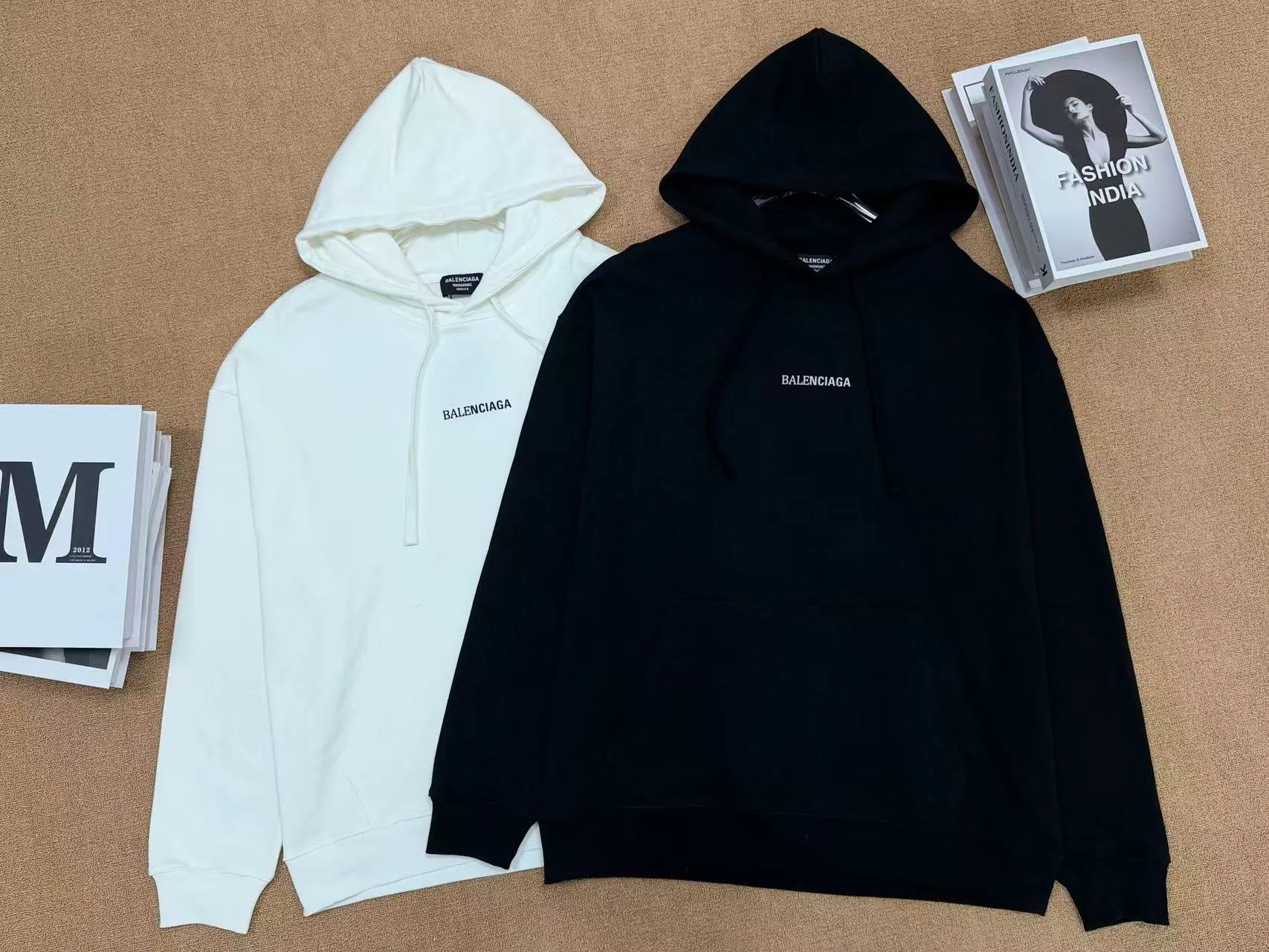 No. 2208 Style: Balenciaga Retro lettered hooded sweatshirt Color: Black, Cream White Version: Oversize loose shoulder, Same style for men and women, lazy and relaxed, covering the flesh and making you look slim Fabric: 430g high gram weight pure cotton terry fabric, soft and thick, with good drape, the upper body is not easy to wrinkle. Design highlights 1. White model: The small logo on the chest is simple and clean, minimalist and low-key style, and the daily Versatile is not picky. 2. Black model: Multi-layered Retro letter printing on the back, white rose red contrasting colors, strong layering, full of trendy atmosphere, the back printing is the visual focus of the entire dress. 3. Classic kangaroo pocket + adjustable drawstring brim, threaded cuffs and hem, Wear-Resistant is not easy to deform, and the workmanship is neatly routed. Wearing scenarios: Suitable for daily outings, commuting, and casual outings. Black is cool and stylish, and looks trendy when paired with jeans, wide-leg pants, and overalls; White is refreshing and simple, suitable for gentle casual style, and can also be worn as a couple's style. Washing and care tips: Machine wash/hand wash with cold water on the reverse side, do not rub the printed area vigorously, and dry in a cool place to avoid exposure to the sun, which may cause the print to crack and fade.